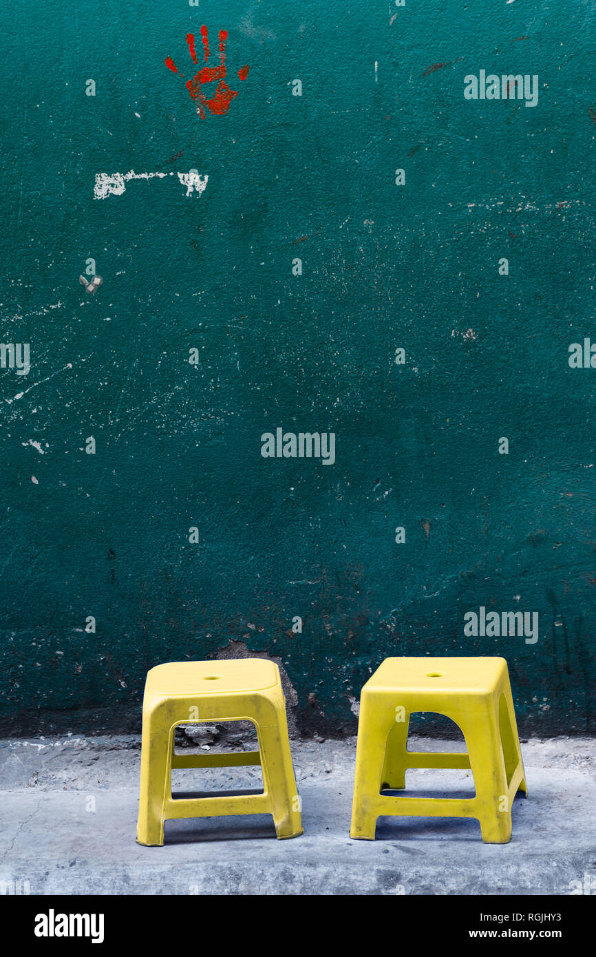 Zwei Blasse gelb Kunststoff Hocker warten Leute auf ihnen auf einer konkreten Seite gehen mit grün gestrichene Wand zu sitzen. Stockfoto