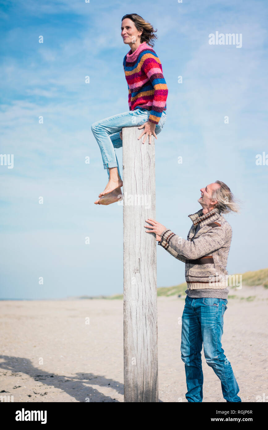 Reifer Mann helfen, Frau Holz Pol am Strand zu klettern Stockfoto