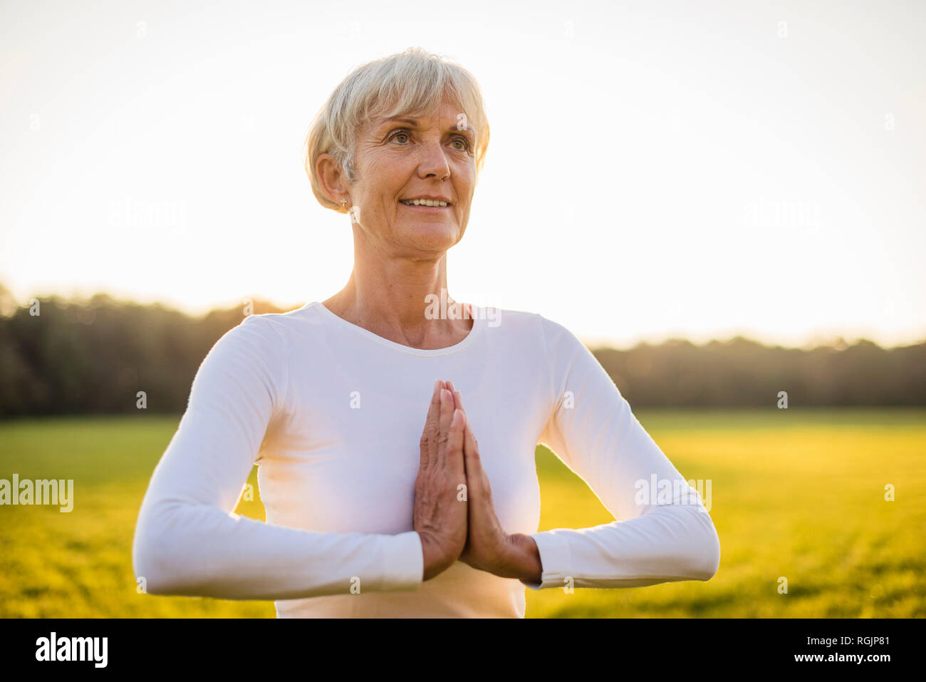 Ältere Frau Yoga auf ländlichen Wiese bei Sonnenuntergang Stockfoto