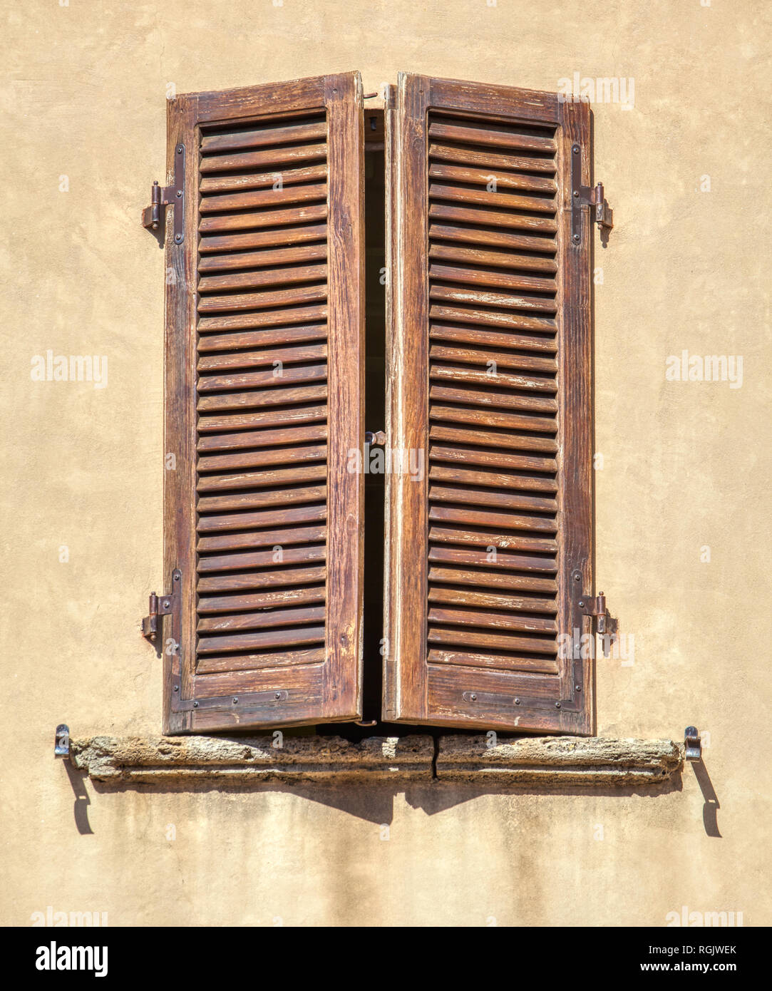 Foto von einem Verwitterten, Holz braun Fensterläden mit schwarzen schmiedeeisernen Scharnieren gegen eine Blasse gelb Putz an der Wand. Stockfoto