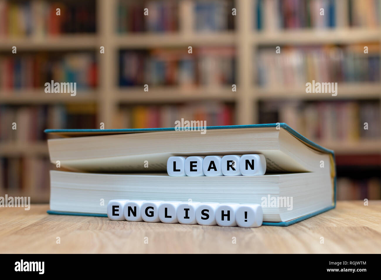 Würfel in ein Buch bilden die Worte "Englisch lernen". Das Buch liegt auf  einem hölzernen Schreibtisch vor einem Bücherregal Stockfotografie - Alamy