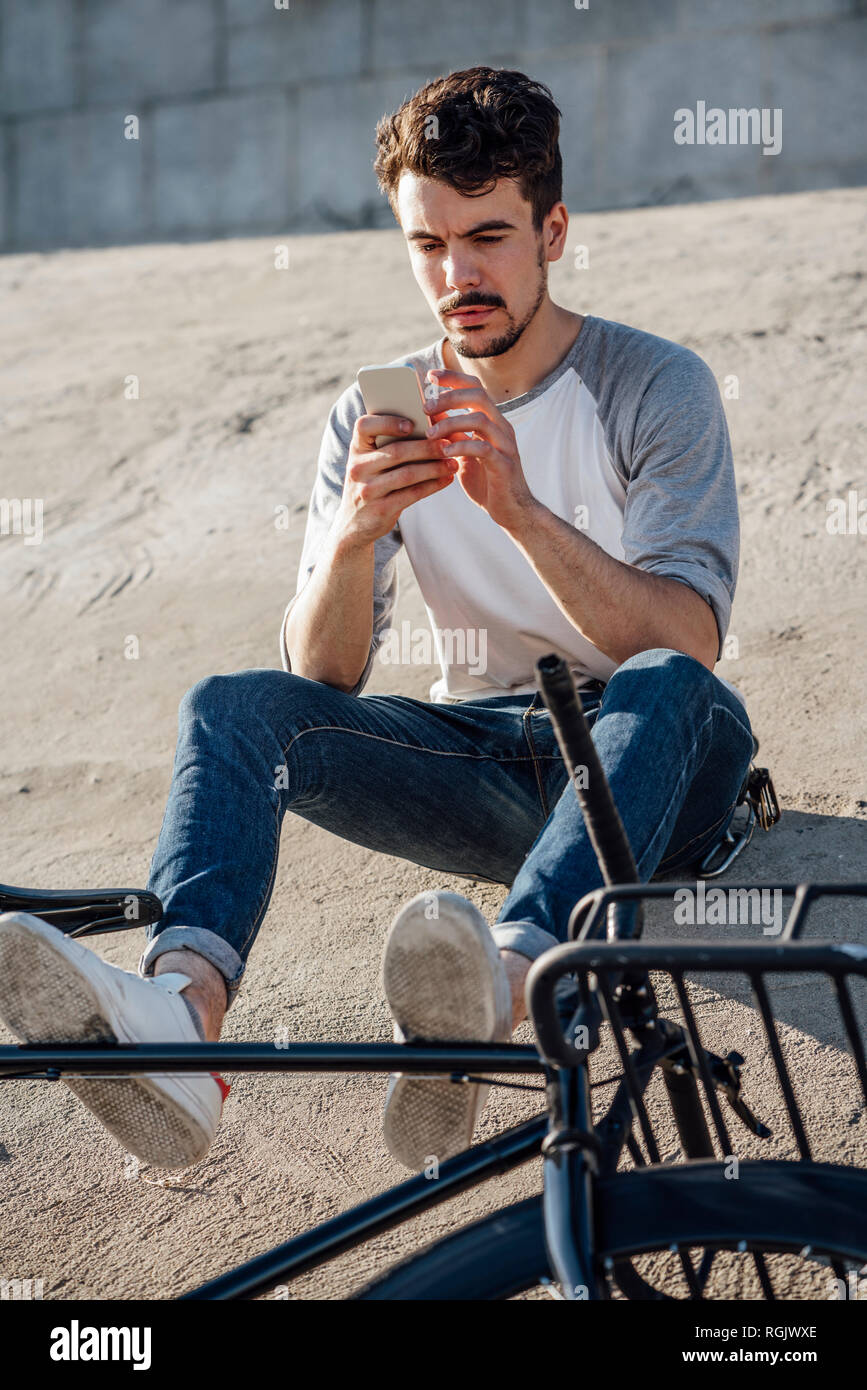 Junger Mann mit Pendler fixie Bike sitzen auf Betonwand mit Handy Stockfoto