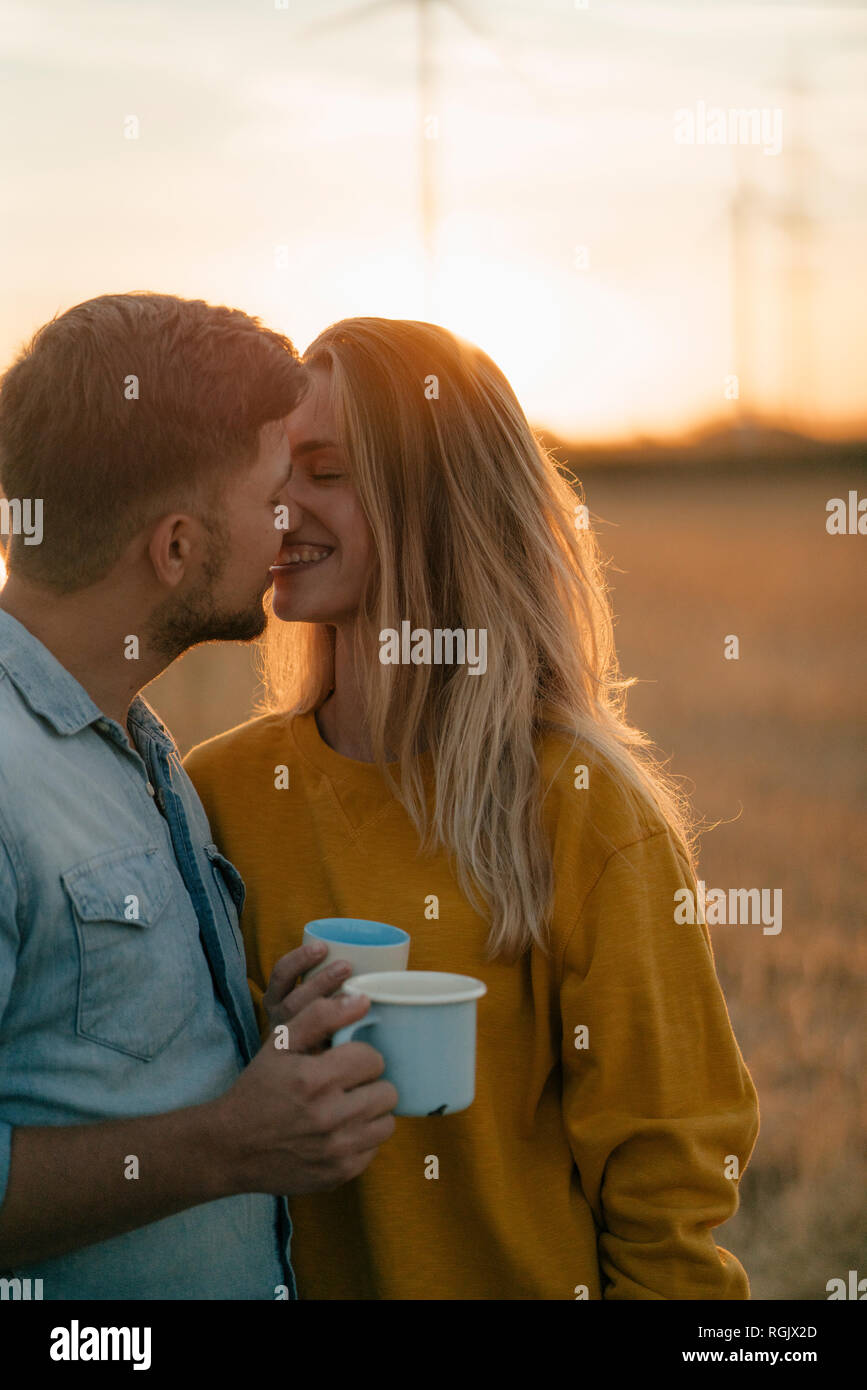 Glückliches junges Paar hält Becher in ländlichen Landschaft küssen Stockfoto