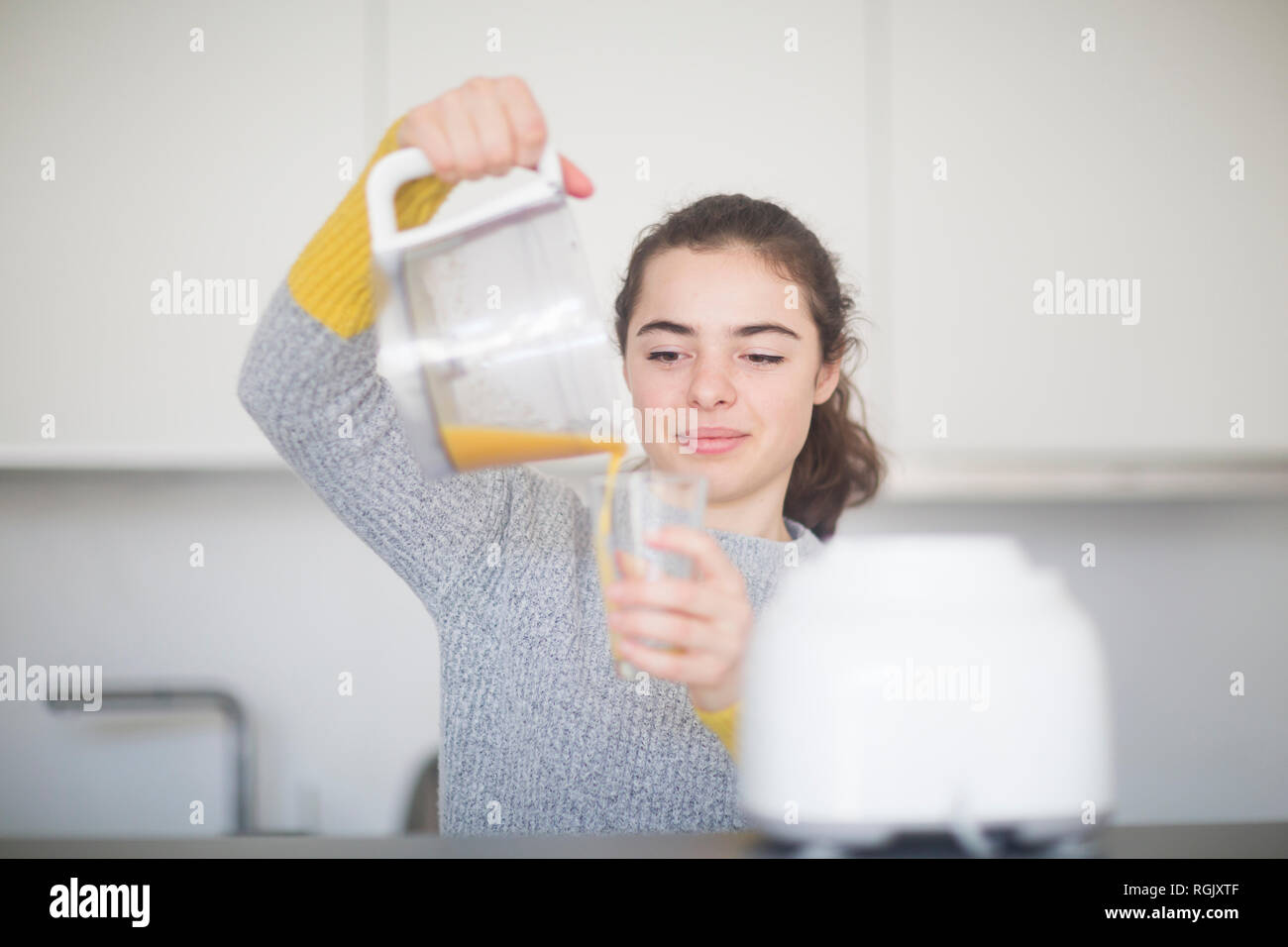 Porträt der lächelnde Frau frisch gepressten Orangensaft in ein Glas in der Küche gießen Stockfoto