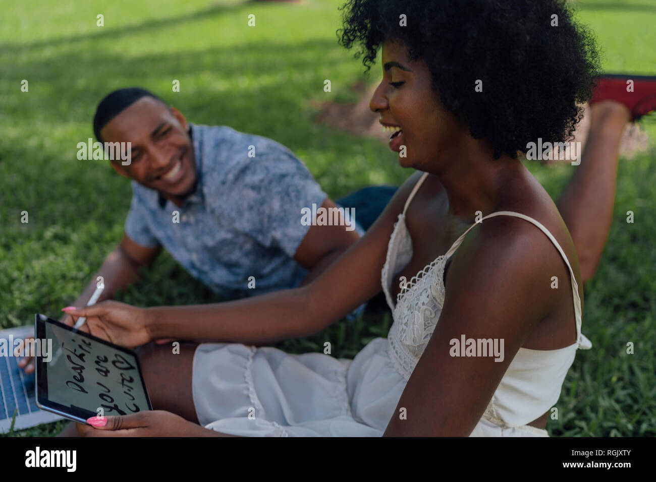 Glückliche junge Frau mit Freund in einem Park mit Tablet Stockfoto