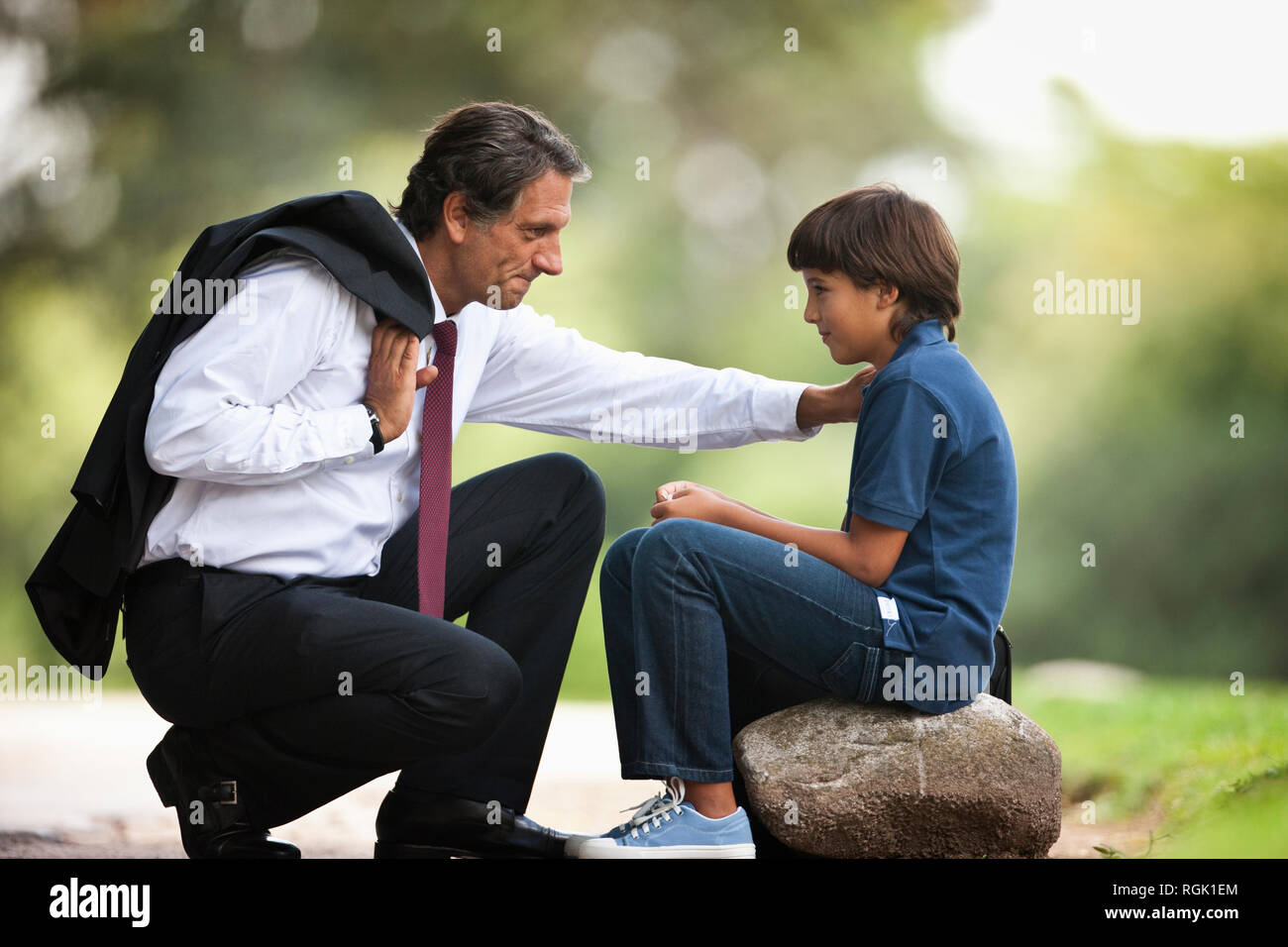 Corporate Mann zusammengekauert neben seinem Sohn auf dem Bürgersteig. Stockfoto