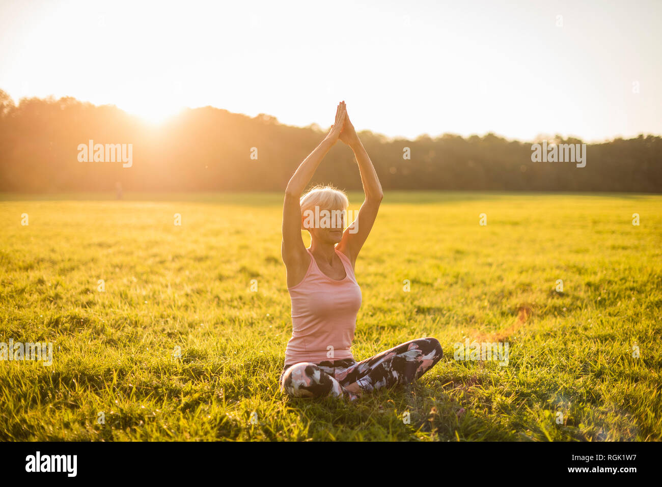 Ältere Frau Yoga auf ländlichen Wiese bei Sonnenuntergang Stockfoto