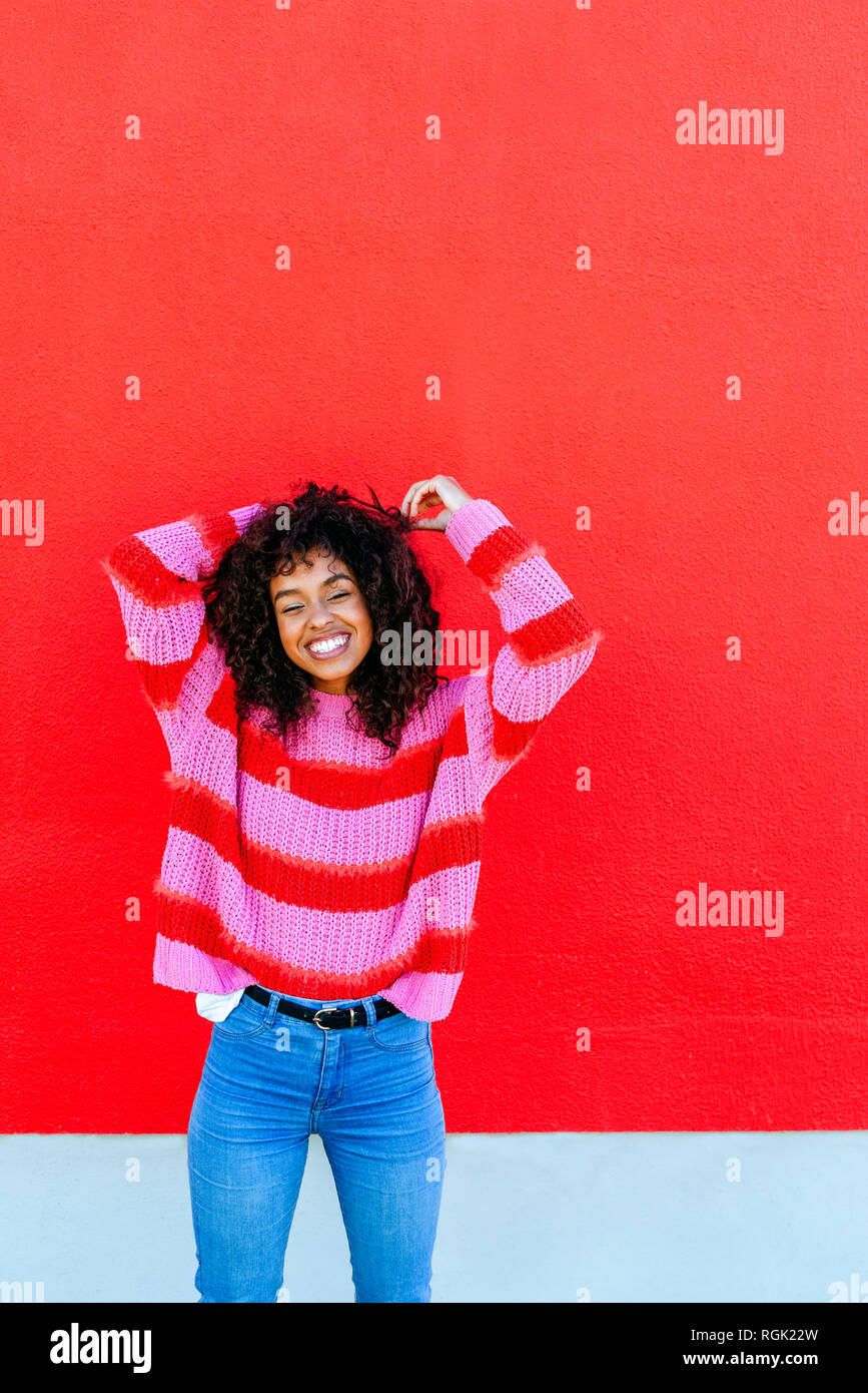 Portrait von Lachende junge Frau mit lockigem Haar stand vor der Roten Wand Stockfoto