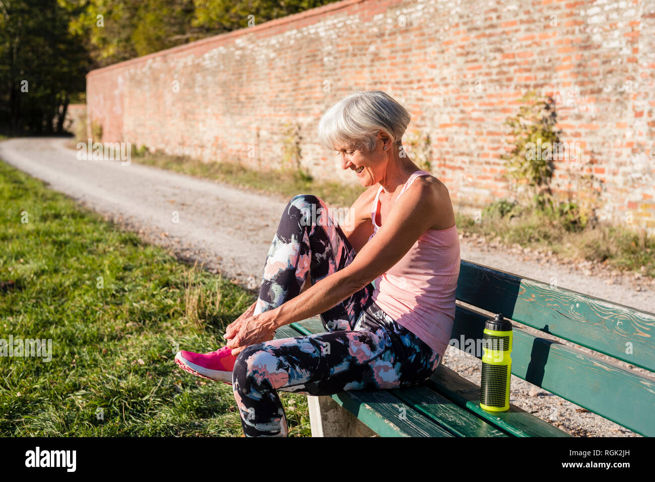 Lächelnd sportliche ältere Frau auf einer Bank sitzen Ihre Schuhe binden Stockfoto