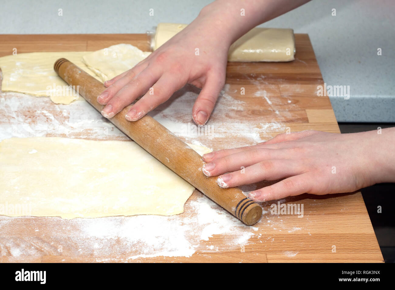 Weibliche Hände mit nudelholz Zubereitung Teig zum backen auf braunem Holz Schneidebrett am Küchentisch. Detailansicht Stockfoto