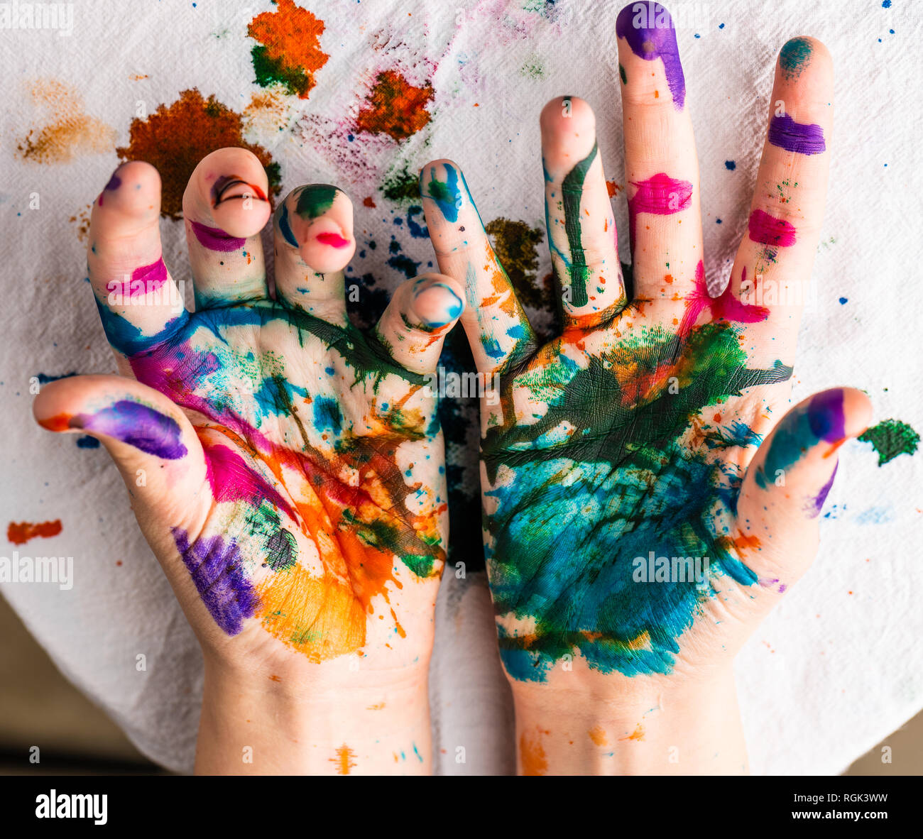 Die Hände des Kindes sind in Rot, Rosa, Gelb, Orange, Rot, Blau, Grün und lila Tinte. Konzepte