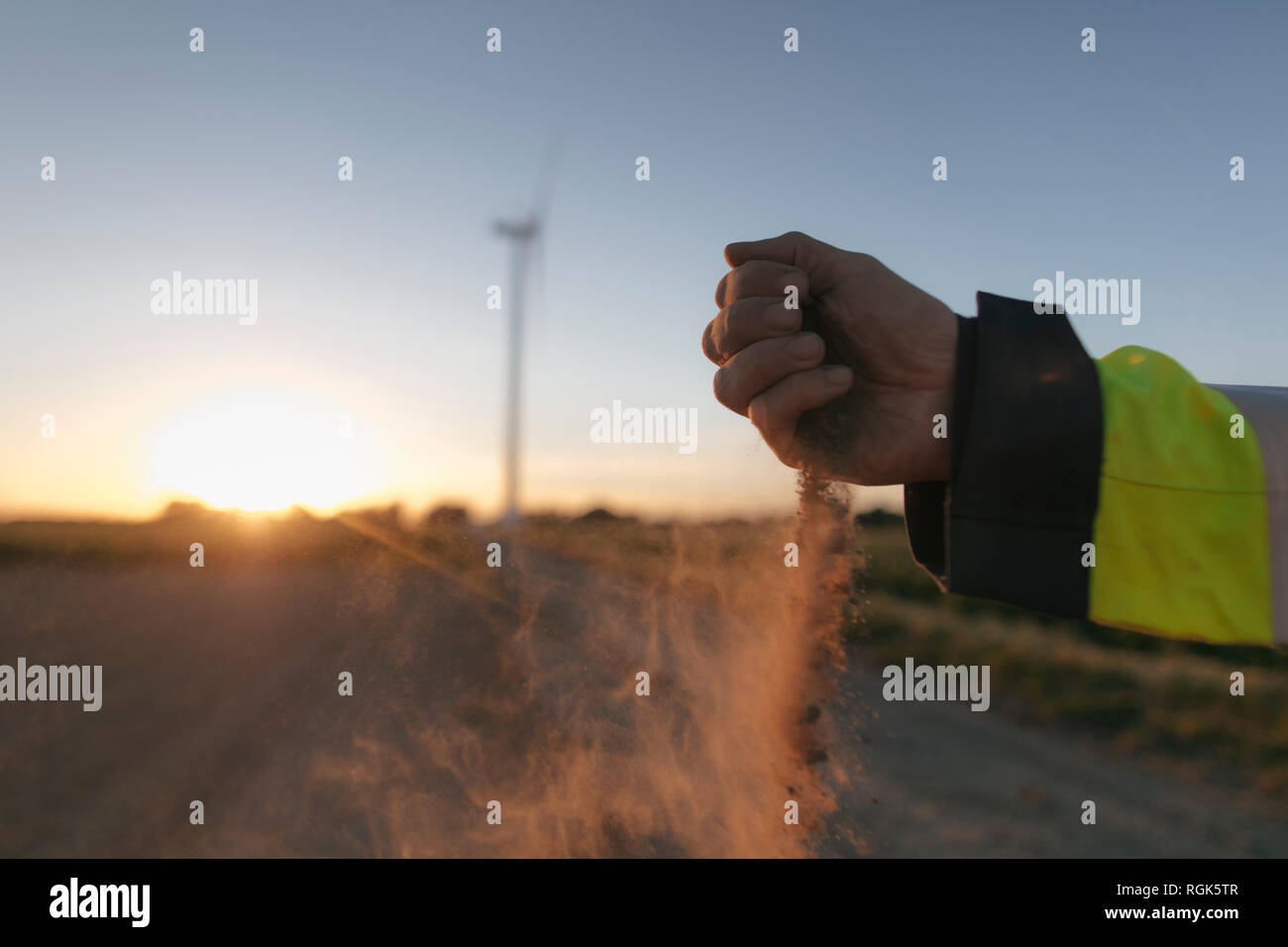 Nahaufnahme der Hand des Menschen Streuung Boden bei Windenergieanlagen bei Sonnenuntergang Stockfoto
