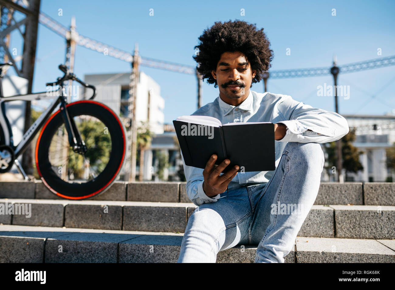 Mitte der erwachsene Mann mit Fahrrad sitzen auf der Treppe, in einem Buch lesend Stockfoto