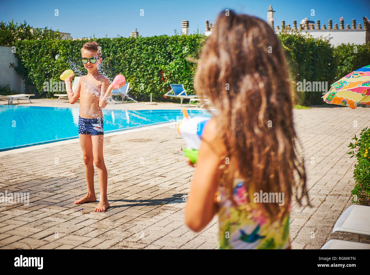 Mädchen mit Wasserpistole Spritzer von Boy holding Wasserbomben an der Poolbar Stockfoto