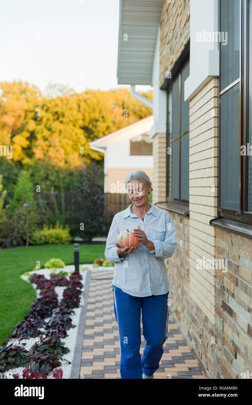 Lächelnde ältere Frau mit Geernteten Kürbis im Garten Stockfoto