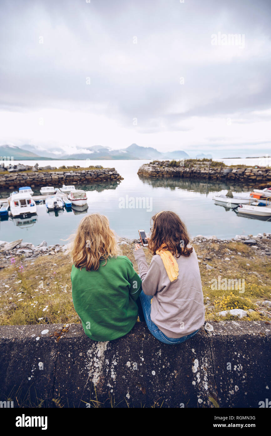 Norwegen, Senja, zwei junge Frau an einem kleinen Hafen mit Handy sitzen Stockfoto