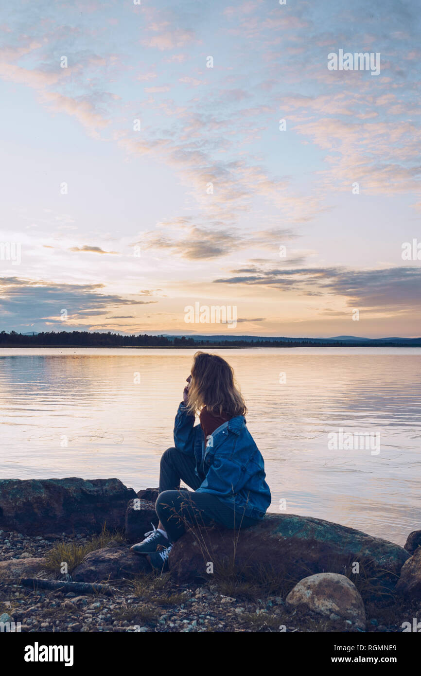 Junge Frau sitzt am See Inari, in Aussicht suchen, Finnland Stockfoto