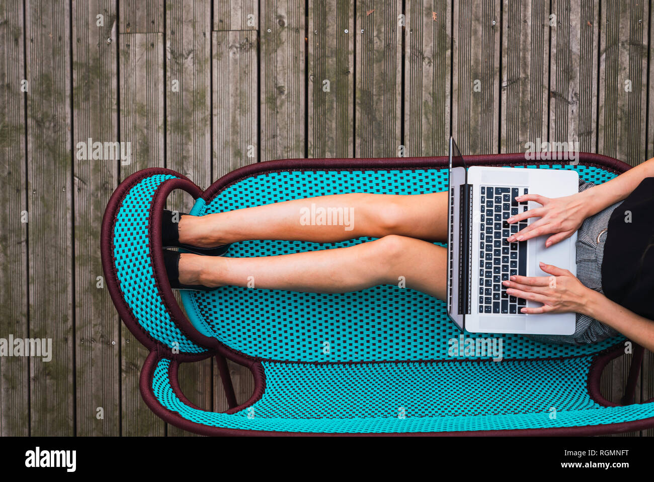 Junge Frau sitzt auf Türkis Tisch auf der Terrasse mit Laptop, Ansicht von oben Stockfoto