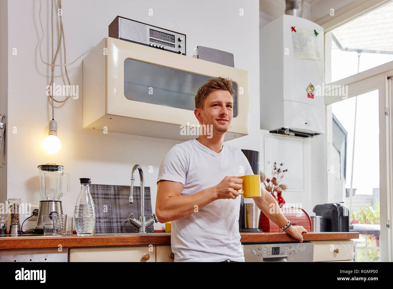 Lächelnden jungen Mann zu Hause in einer Kaffeepause in der Küche Stockfoto