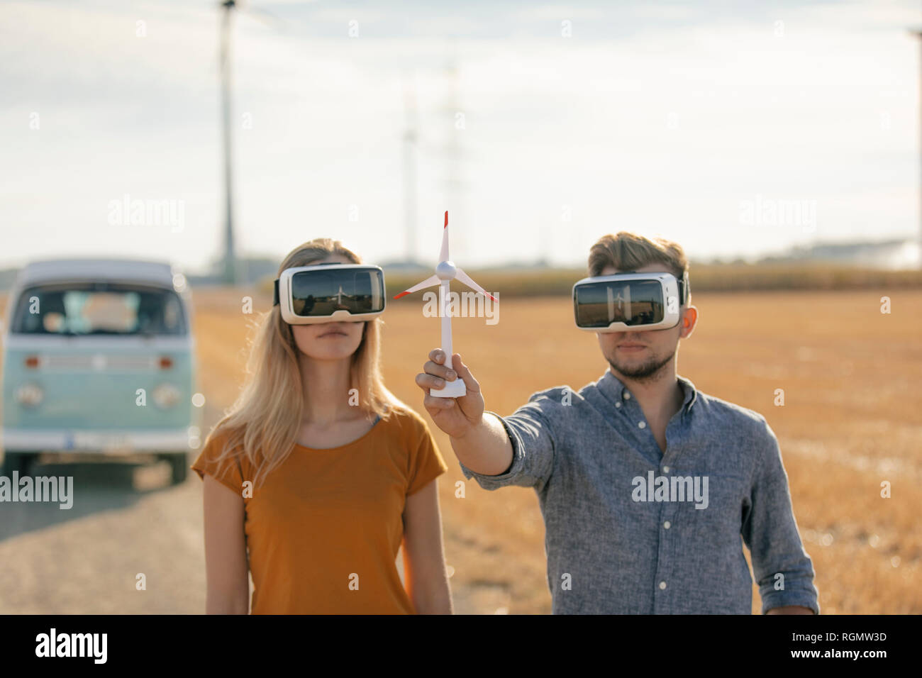 Junges Paar mit VR-Brille im Wohnmobil in ländlichen Landschaft Holding wind turbine Modell Stockfoto