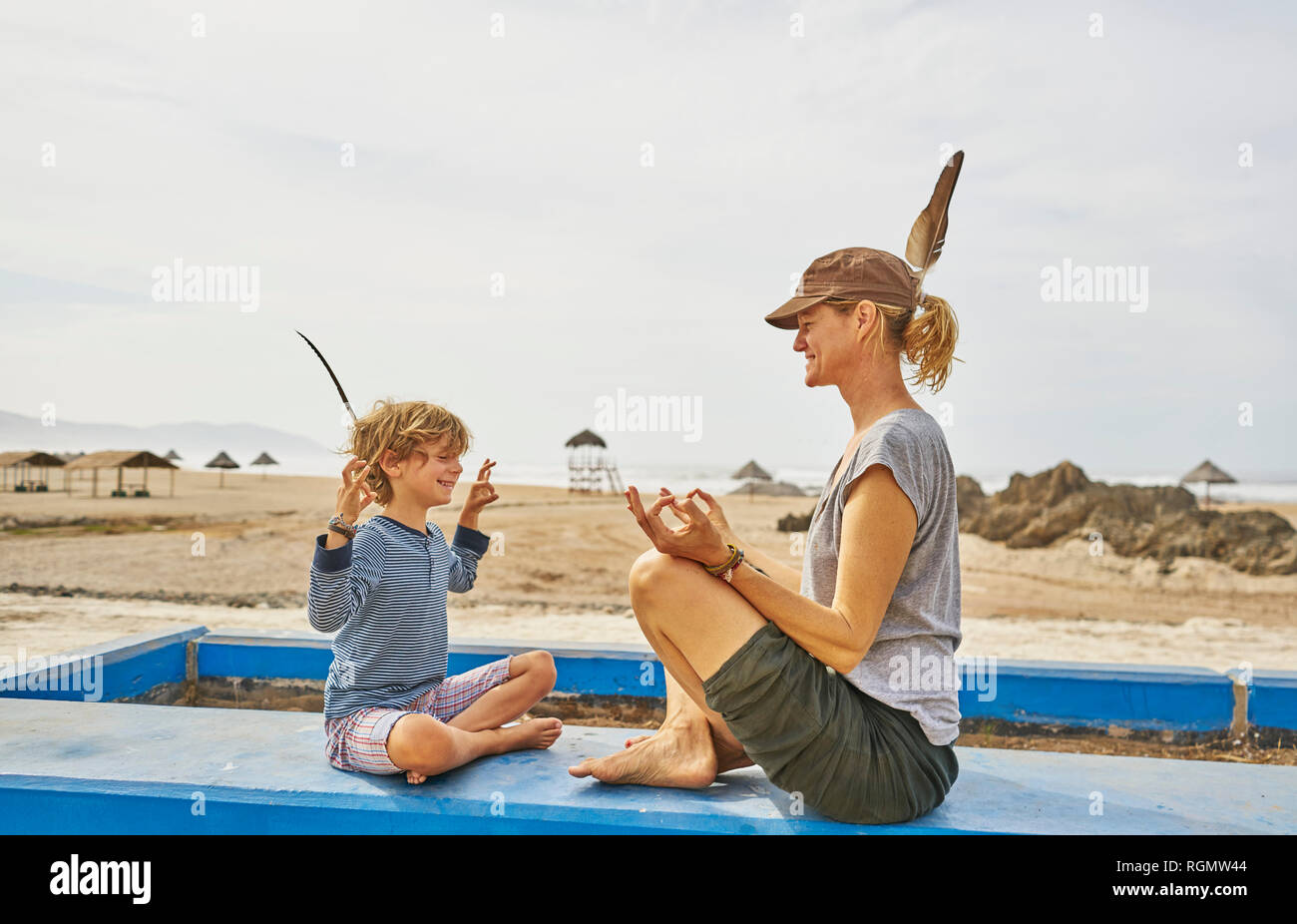 Chile, Arica, glückliche Mutter in Yoga pose sitzend mit Sohn an der Wall am Strand Stockfoto