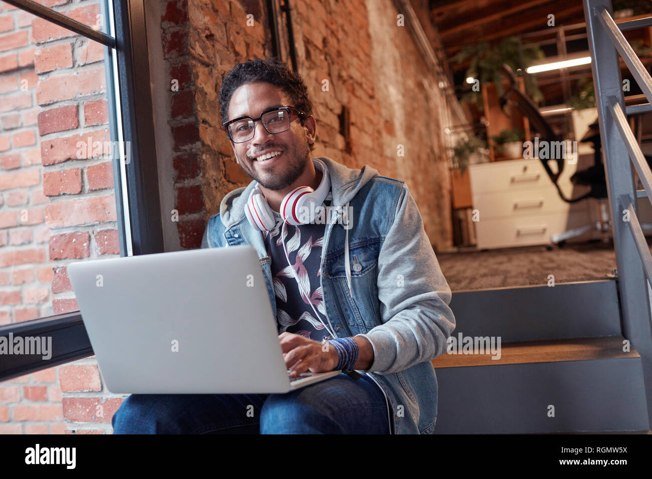 Junger Mann mit Ohrhörer sitzen auf Office Treppen, mit Laptop Stockfoto