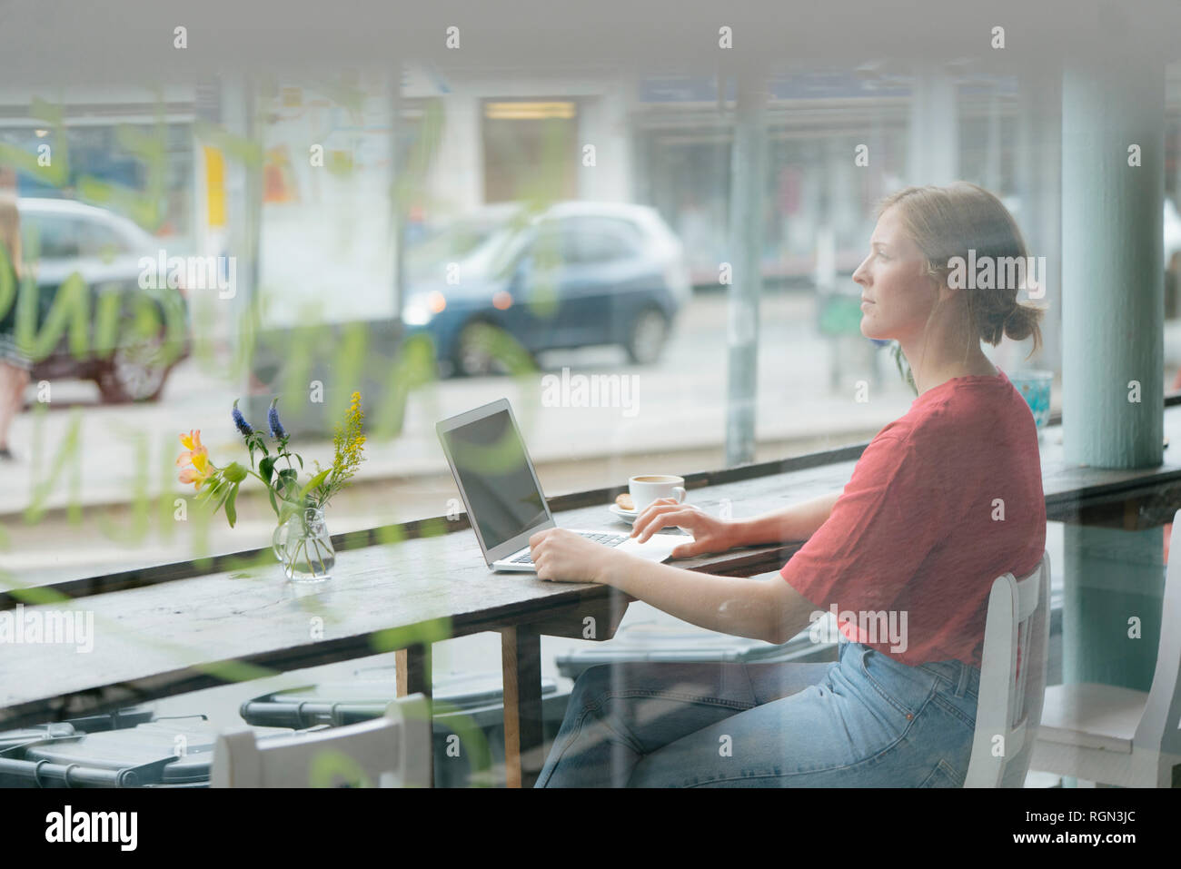 Junge Frau mit Tasse Kaffee und Laptop am Fenster sitzen in einem Cafe Stockfoto