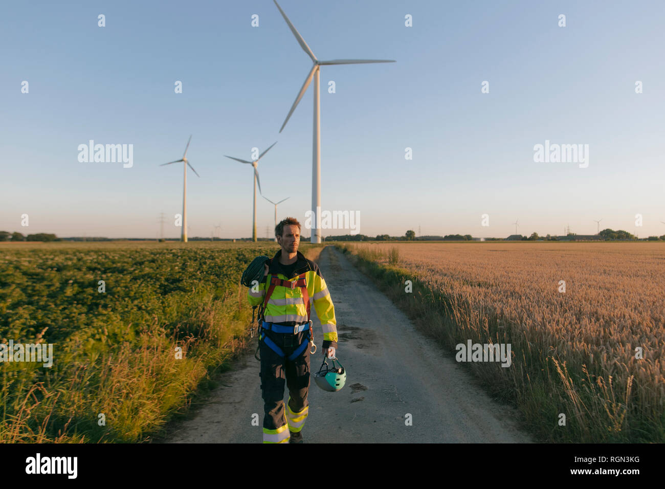 Techniker gehen auf Feld Pfad in einen Windpark mit Kletterausrüstung Stockfoto