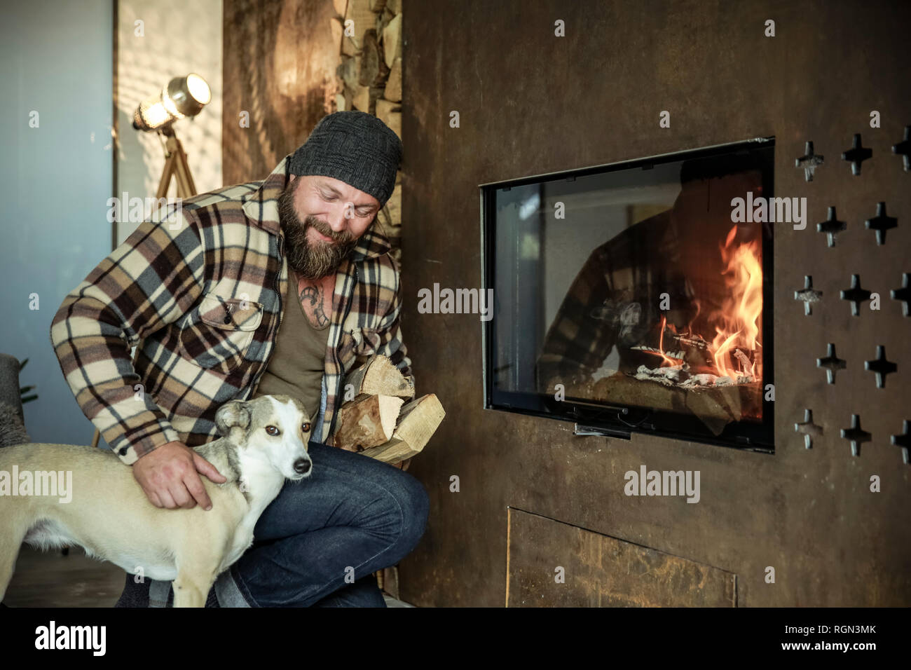 Bärtiger Mann mit seinem Hund vor dem Kamin zu Hause Stockfoto