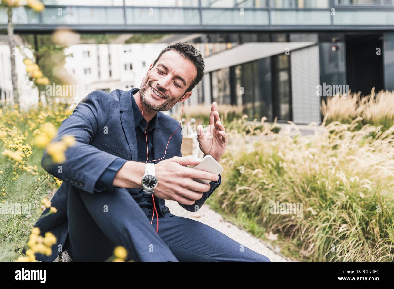Geschäftsmann, draußen zu sitzen, einen Bruch, hören Musik aus seinem Smartphone Stockfoto