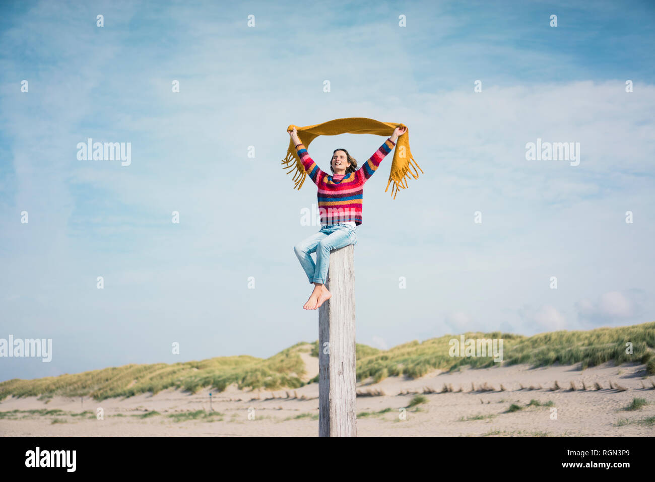 Reife Frau sitzt auf einem Holz Pol am Strand, holding Schal im Wind Stockfoto