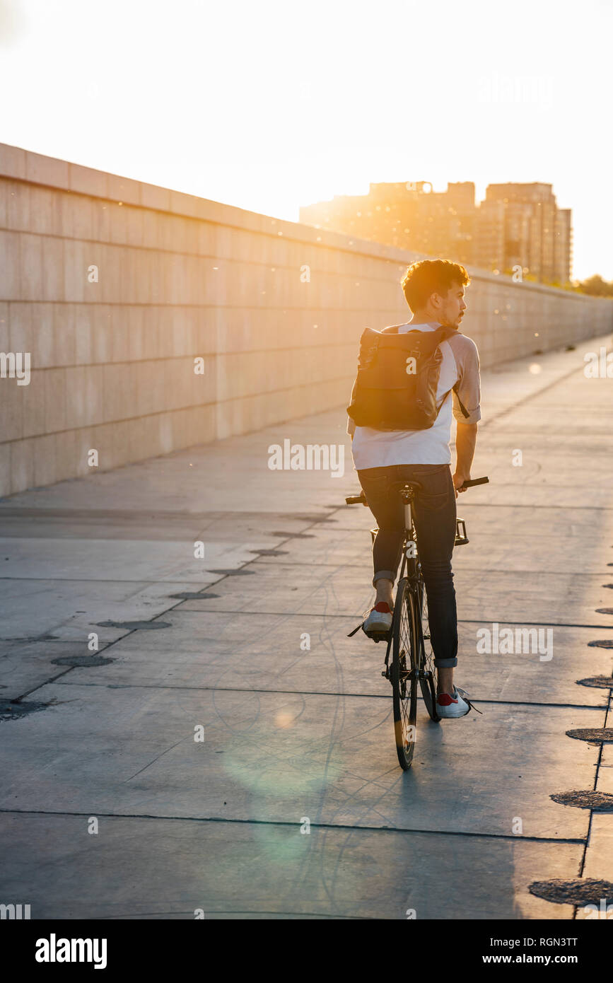 Junger Mann mit Rucksack, Fahrrad an der Promenade bei Sonnenuntergang Stockfoto