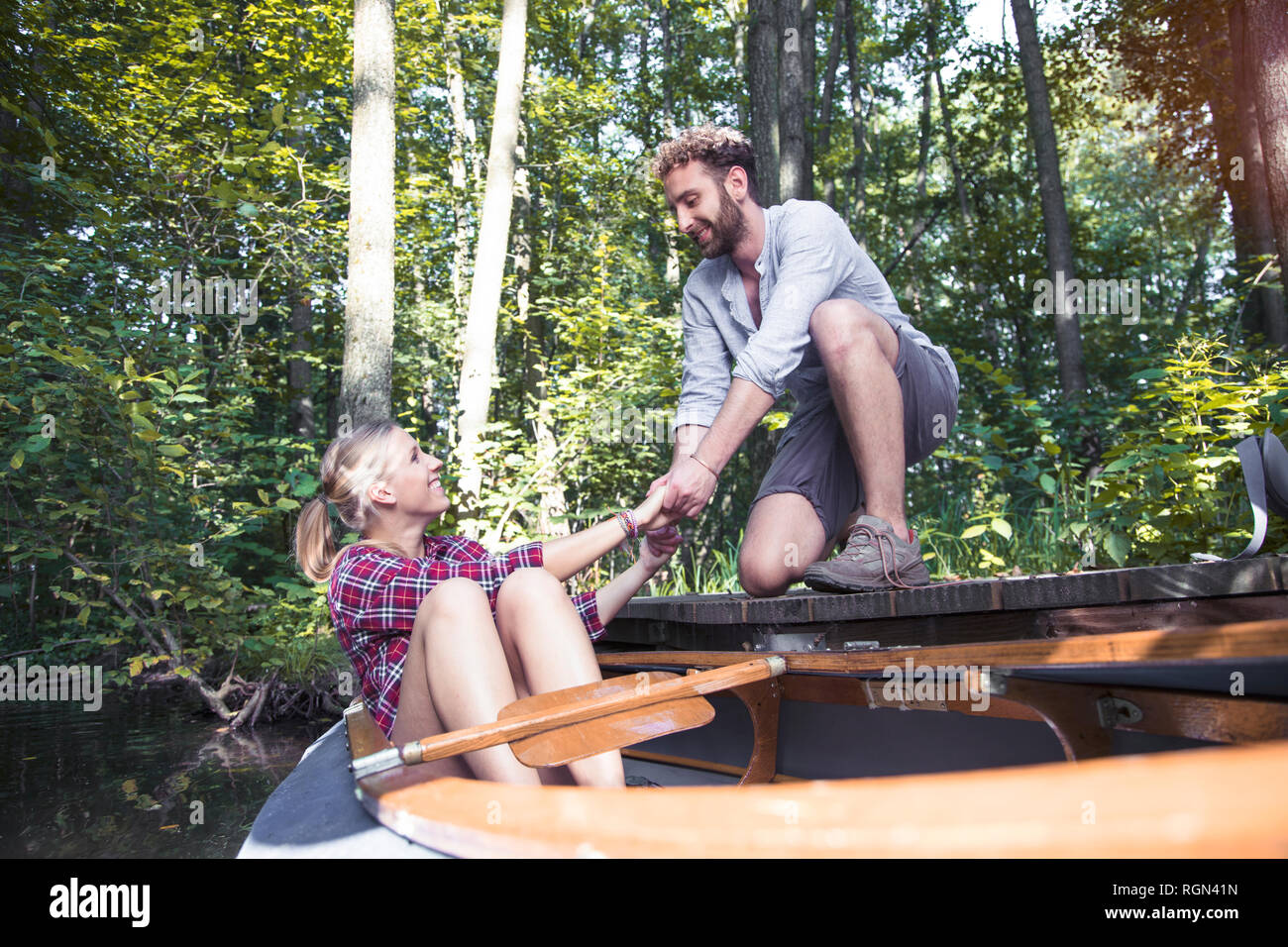 Lächelnden jungen Mann helfen Freundin aus einem Kanu in einem Wald Bach Stockfoto