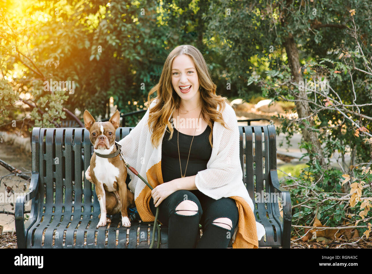 Eine weiße Frau sitzt neben Ihrem Hund auf einer Parkbank die Sonne hinter Sie sehr glücklich Stockfoto