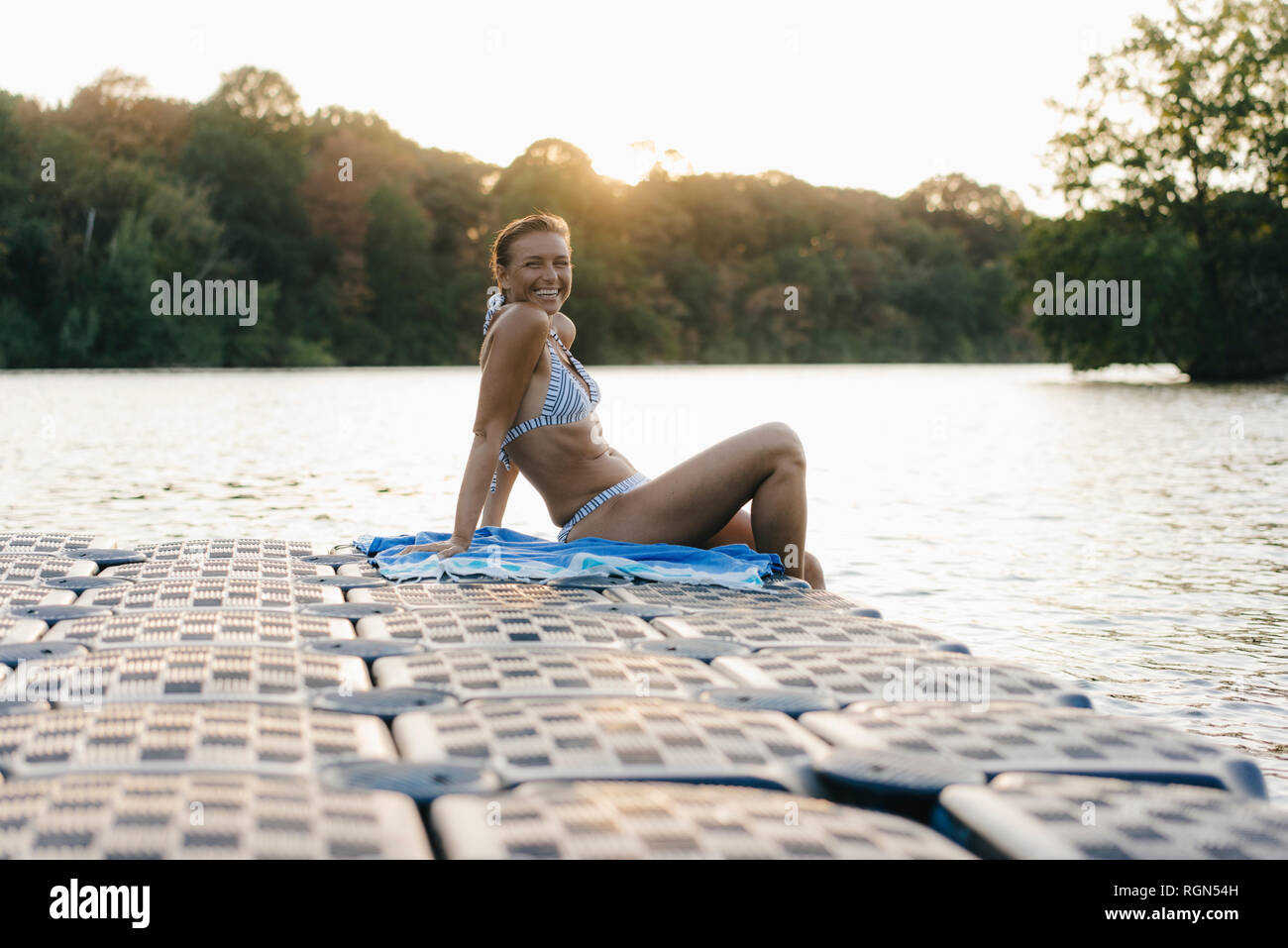 Glückliche Frau trägt einen Bikini sitzt auf einem Schwimmer, der an einem See Stockfoto