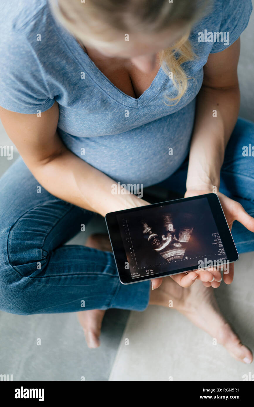 Schwangere Frau auf dem Boden sitzend mit Ultraschall Bild auf Tablet Stockfoto