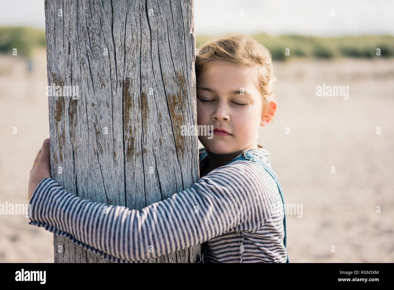 Kleines Mädchen umarmt Holz Pole mit geschlossenen Augen Stockfoto