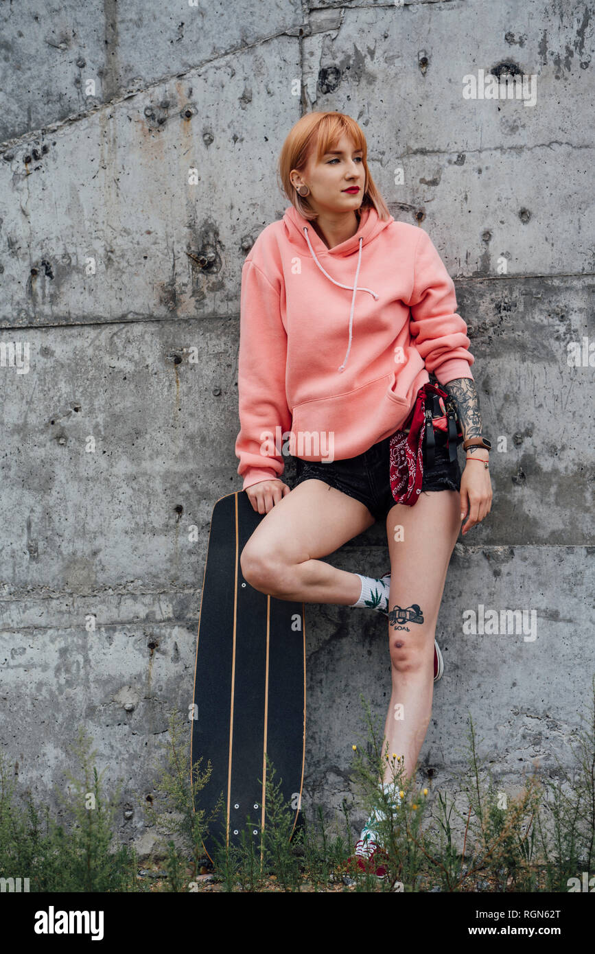 Portrait von Cool junge Frau mit Carver skateboard lehnte sich gegen eine Betonwand Stockfoto