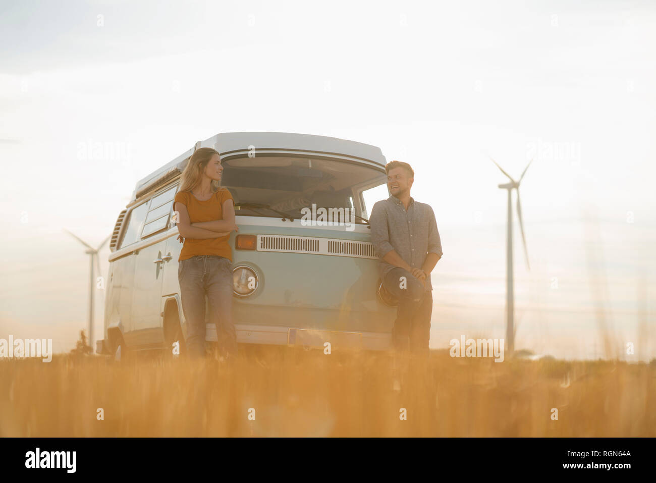 Glückliches Paar an Wohnmobil in ländlichen Landschaft mit Windkraftanlagen im Hintergrund Stockfoto