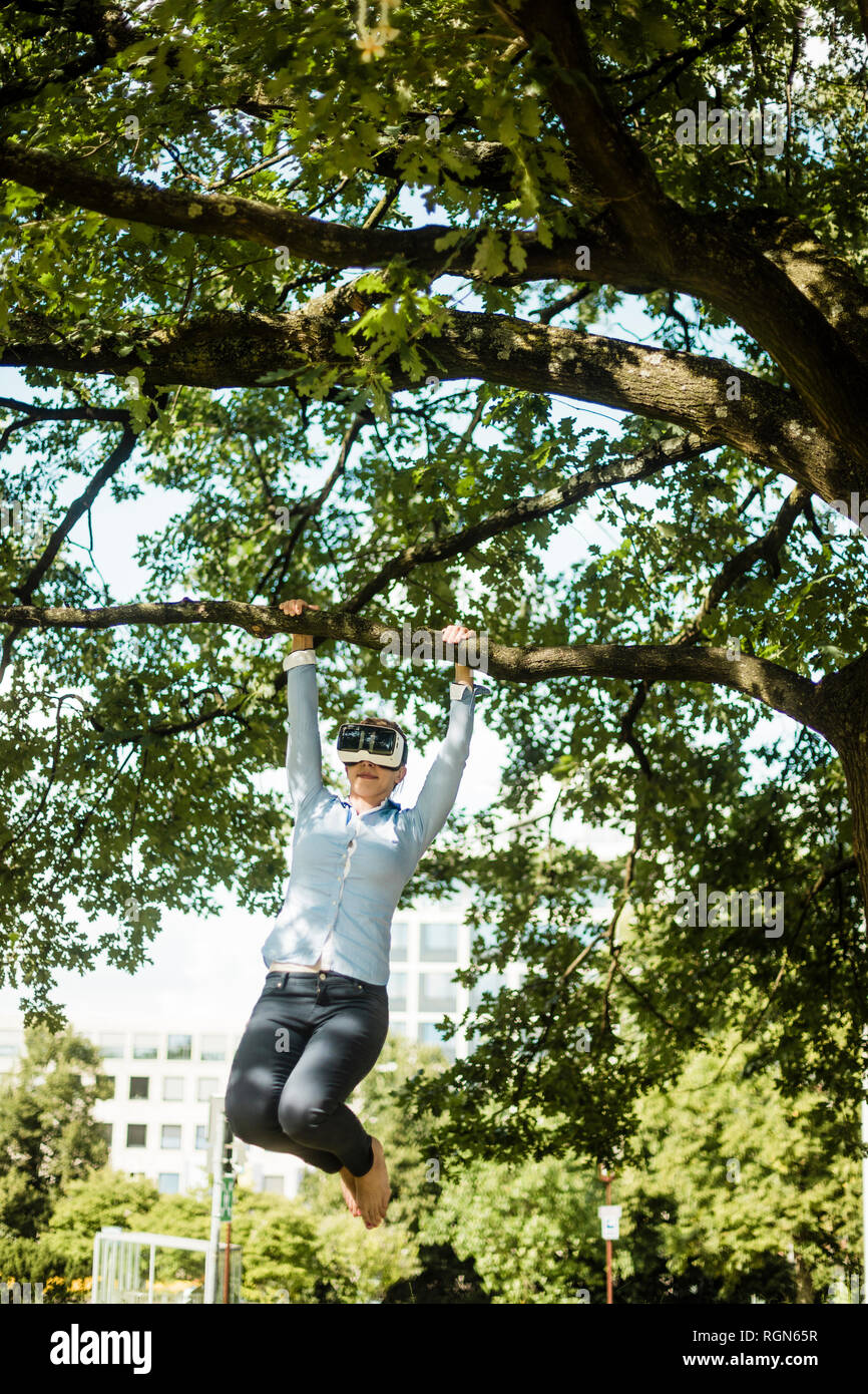 Frau in städtischen Park hängt am Ast eines Baumes tragen VR-Brille Stockfoto