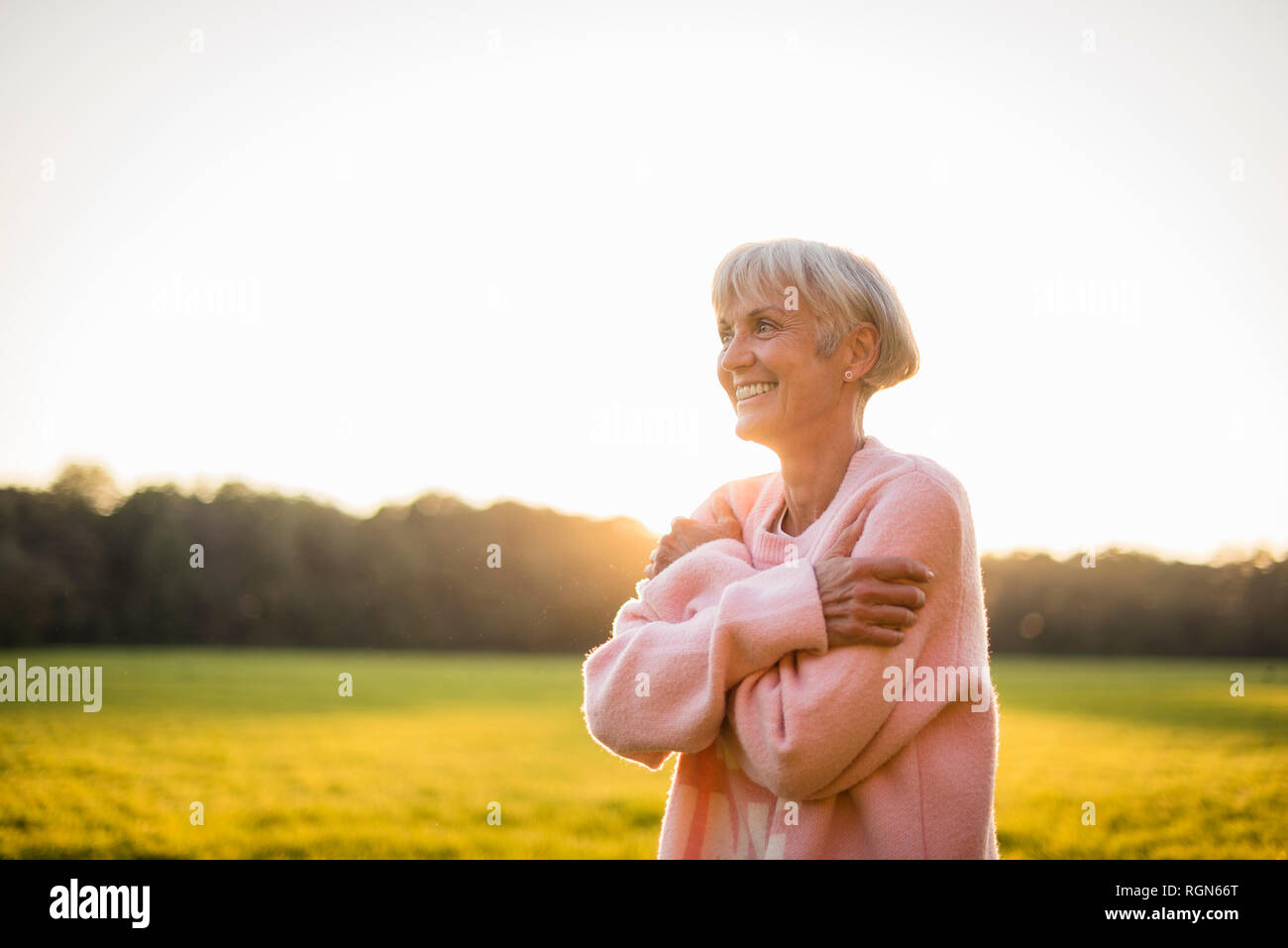 Lächelnde ältere Frau, die auf den ländlichen Wiese bei Sonnenuntergang Stockfoto