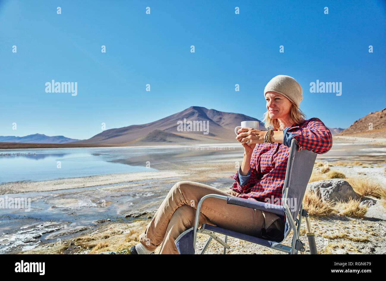 Bolivien, Laguna Colorada, Frau sitzt auf Camping Stuhl am Seeufer das Trinken aus dem Becher Stockfoto