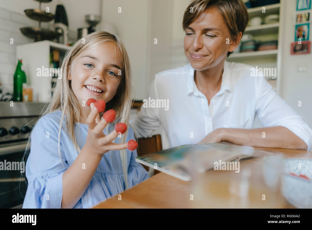 Glückliche Mutter und Tochter sitzen am Tisch in der Küche zu Hause spielt mit Himbeeren Stockfoto