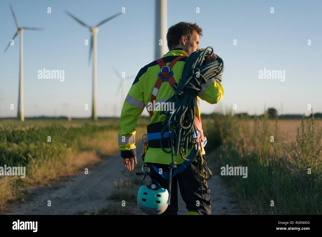 Techniker gehen auf Feld Pfad in einen Windpark mit Kletterausrüstung Stockfoto