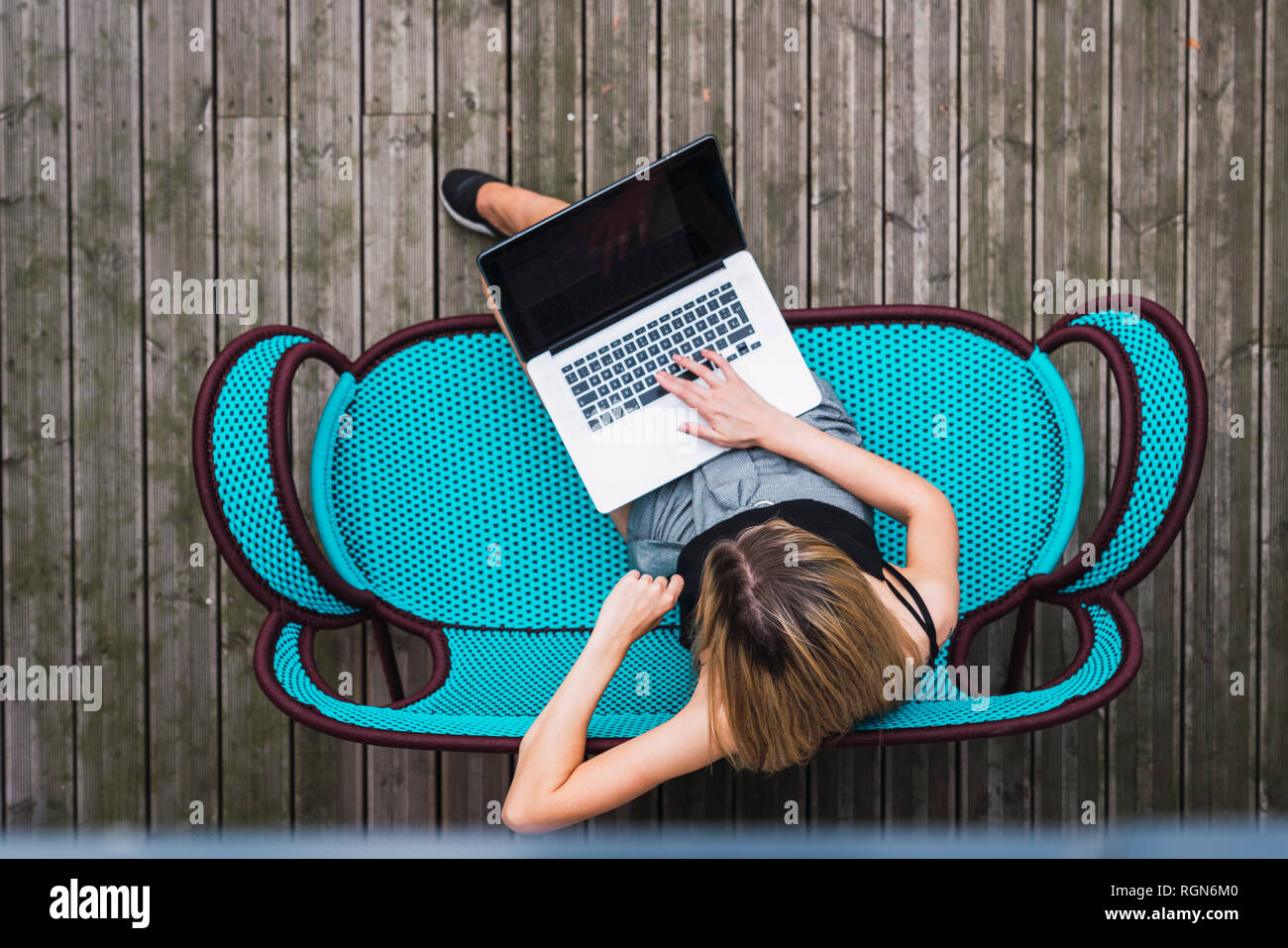 Junge Frau sitzt auf Türkis Tisch auf der Terrasse mit Laptop, Ansicht von oben Stockfoto