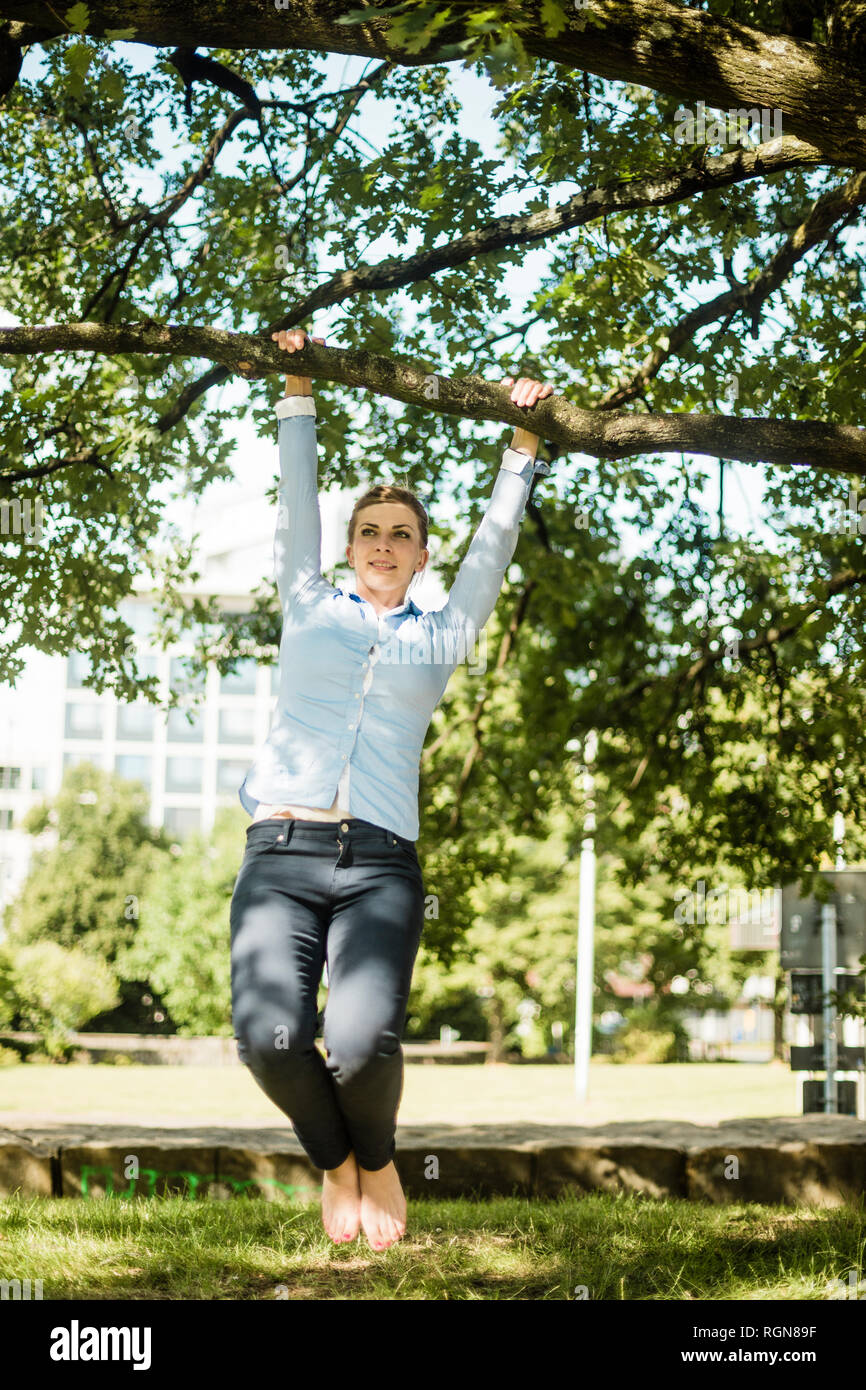 Frau in städtischen Park hängt am Ast eines Baumes Stockfoto