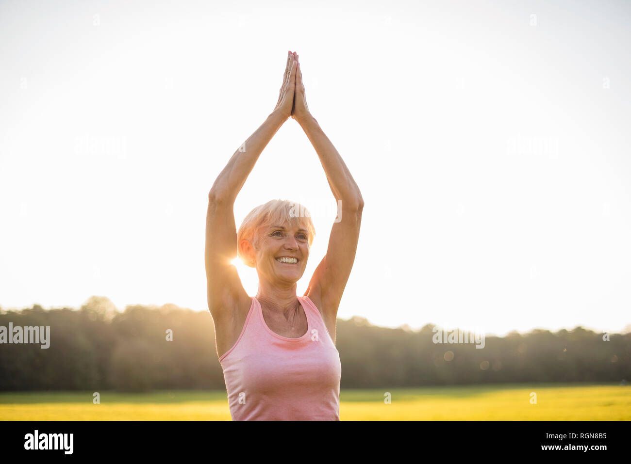 Lächelnd senior frau yoga auf ländlichen Wiese bei Sonnenuntergang Stockfoto