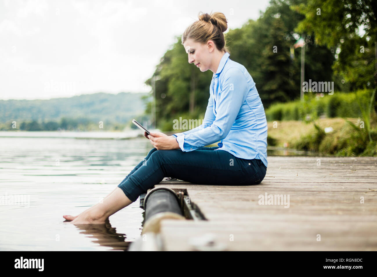 Frau sitzt auf der Jetty an einem See mit Tablet Stockfoto