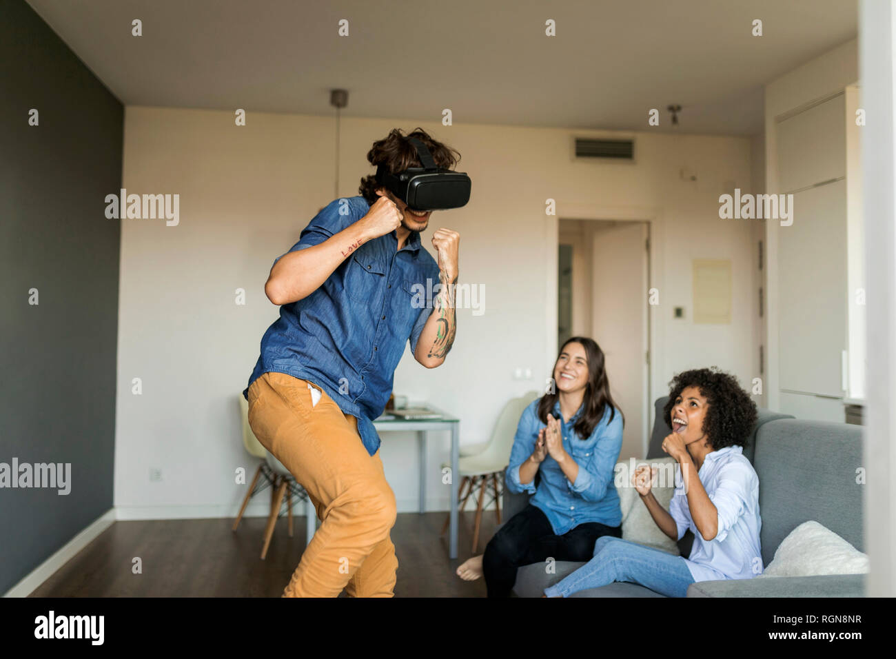 Zwei Frauen Förderung mann Gaming mit VR-Brille zu Hause Stockfoto