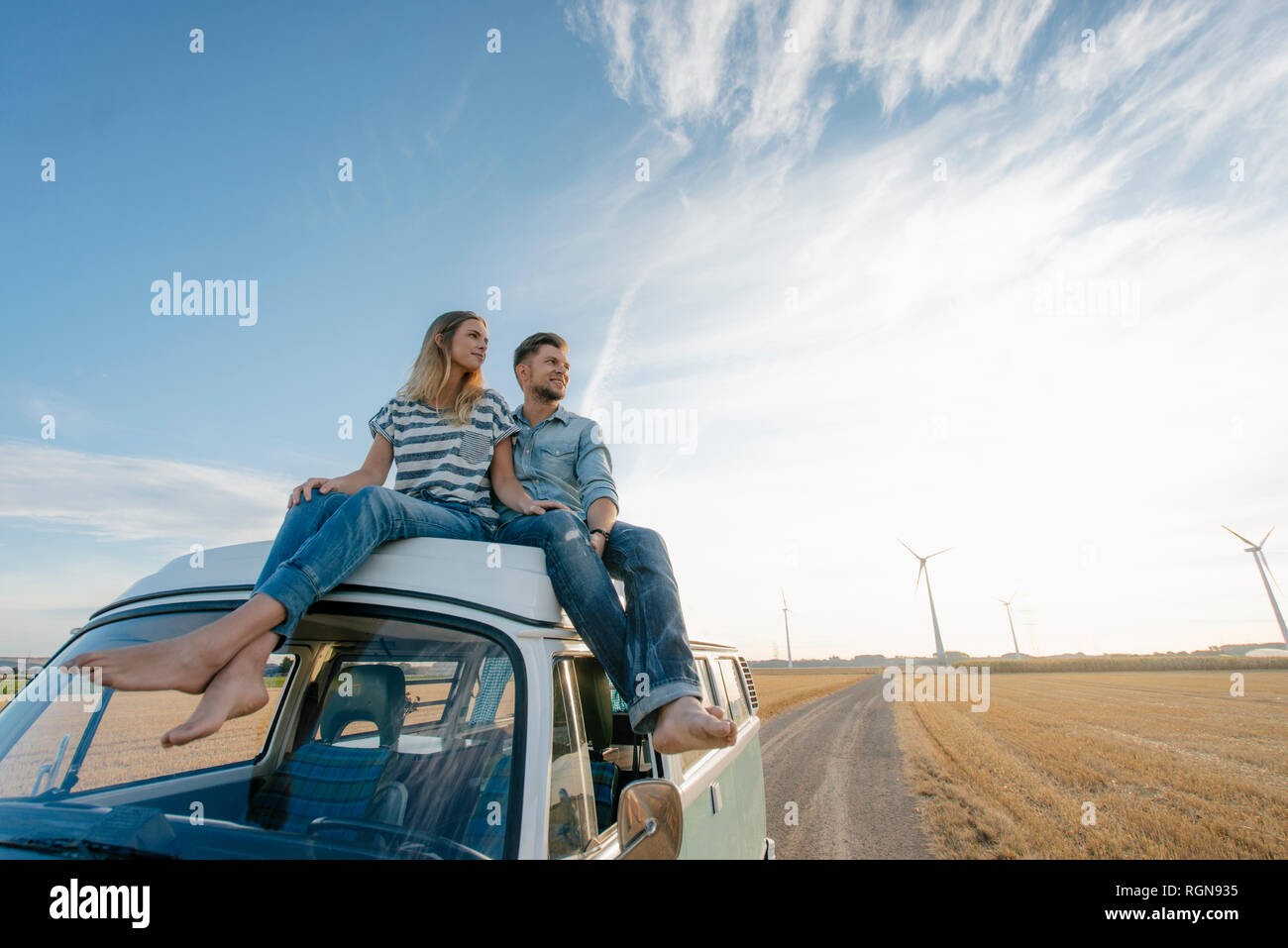 Paar sitzt auf Wohnmobil in ländlichen Landschaft mit Windkraftanlagen im Hintergrund Stockfoto